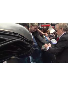 Ridley Scott firma un DVD de Alien mientras un Alien le vigila en la alfombra azul de la Premiere de Prometheus en Londres